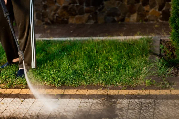 Tutup foto seorang pria tangan, membersihkan genteng rumput di halamannya. Pembersihan tekanan tinggi — Stok Foto