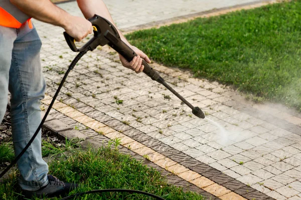 Seorang pria dalam rompi oranye membersihkan genteng rumput di halamannya. Pembersihan tekanan tinggi — Stok Foto