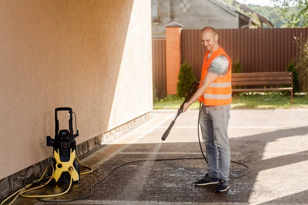 Ein Mann in orangefarbener Weste säubert in seinem Hof in der Nähe des Hauses eine Rasenfläche. Hochdruckreinigung lizenzfreie Stockfotos