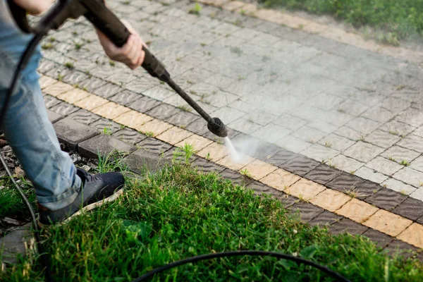 Närbild foto av en man händer, rengör en bricka med gräs på sin gård. Högtrycksrengöring Stockbild