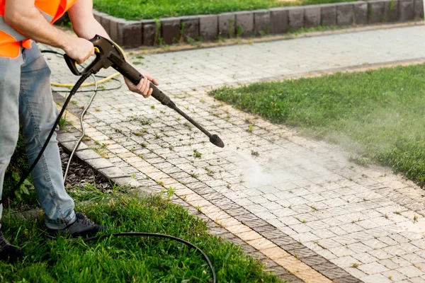 A man in an orange vest cleans a tile of grass in his yard. High pressure cleaning Stock Image
