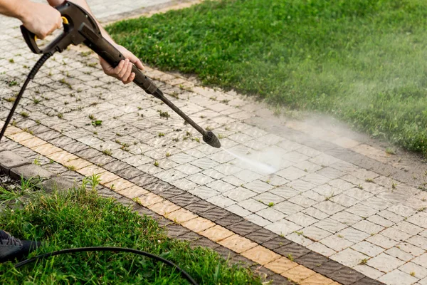 Tutup foto seorang pria tangan, membersihkan genteng rumput di halamannya. Pembersihan tekanan tinggi Stok Foto Bebas Royalti