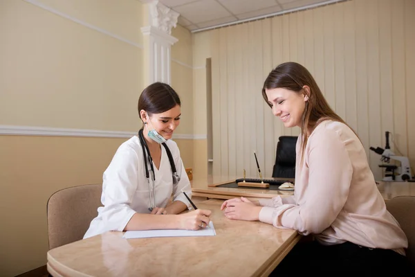 Dokter perempuan duduk di meja di kantor dan menulis resep untuk pasien . — Stok Foto