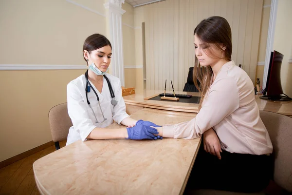 Dokter wanita dengan stetoskop di leher dan sarung tangan biru mengukur denyut nadi pasien . — Stok Foto