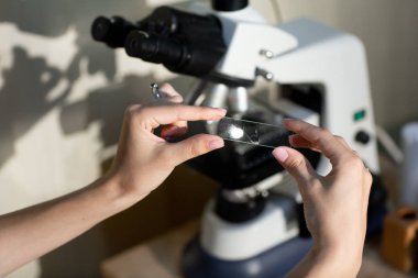 Beyaz tıbbi üniformalı kadın ellerini yaklaştır, örnek analizi yapılan bir cam parçasını tut. Testler, sağlık kontrolleri