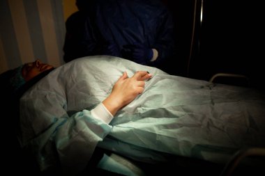 Cerrah ve hasta ameliyathanede. Ameliyat masasında yatan bir kadın ameliyattan önce şans dilemek için dua eder. Kapat.