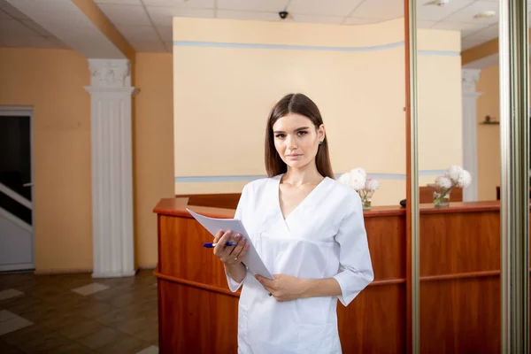 Potret dokter wanita yang percaya diri, dengan kertas di tangan, mengenakan seragam putih. Mempersiapkan kunjungan pasien. . — Stok Foto