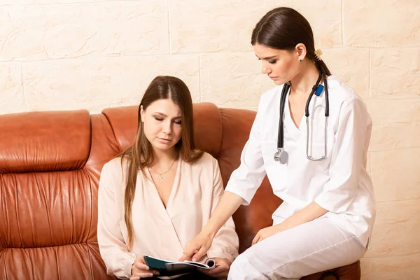 Dokter wanita menyarankan pasien setelah masuk. Wanita duduk di sofa di ruang resepsionis yang nyaman dan berbicara — Stok Foto