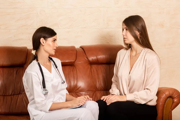 Dokter wanita menyarankan pasien setelah masuk. Wanita duduk di sofa di ruang resepsionis yang nyaman dan berbicara — Stok Foto