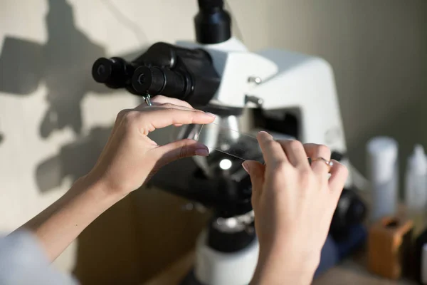 Luk op af kvindelige hænder i hvid medicinsk uniform, hold et stykke glas med prøve analyse. Undersøgelser, sundhedstjek - Stock-foto