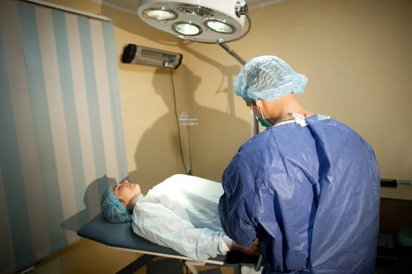 The surgeon stands with his back to the camera. Before him on the operating table lies a patient. Preparation for surgery