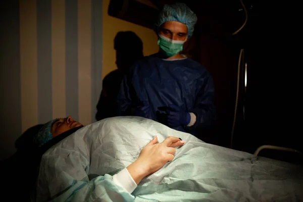 Ahli bedah dan pasien di ruang operasi. Seorang wanita berbaring di meja operasi dan menyilangkan jarinya untuk keberuntungan sebelum operasi. Tutup. — Stok Foto