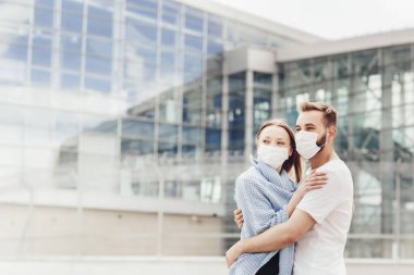 Koronavirüs karantinasından sonra koruyucu maskeli mutlu bir adam ve kadın uçağın inişini izliyor. Havaalanı yakınında genç bir çift, hava yolculuğu, seyahat konsepti.