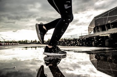 Spor geçmişi. Hareket halindeki bir koşucunun güçlü atletik bacakları. Yağmurdan sonra dışarıda kardiyo çalışması yapan bir kadın..
