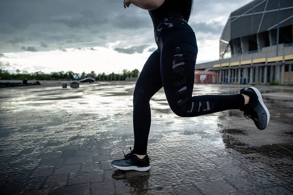 Sports background. Strong athletic legs of a woman runner in motion. Morning workouts outdoors after the rain. Woman preparing for a marathon.