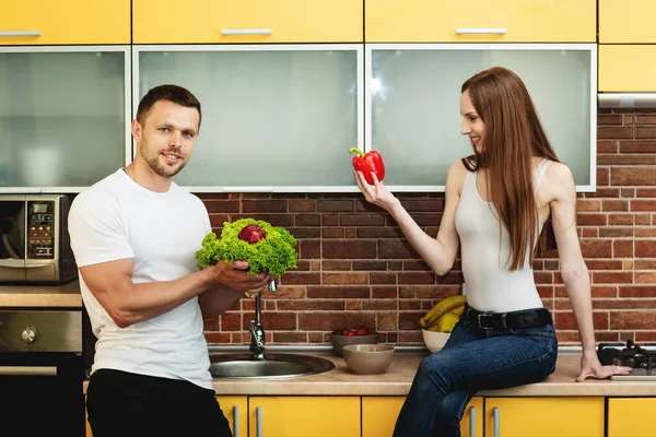 Pemuda menarik pria dan wanita di dapur memegang sayuran dan buah-buahan. Konsep makanan sehat. — Stok Foto