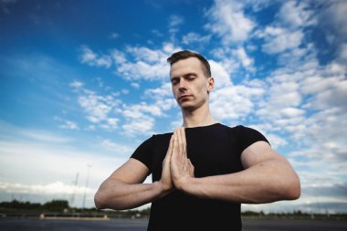 Mavi gökyüzünde bulutlarla yoga yapan genç bir adamın yakın plan portresi..