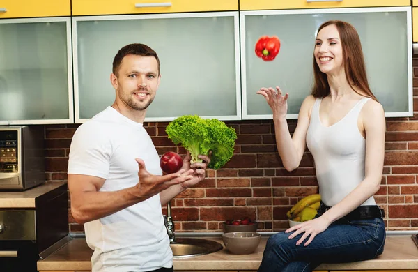Pemuda menarik pria dan wanita di dapur memegang sayuran dan buah-buahan. Konsep makanan sehat. — Stok Foto