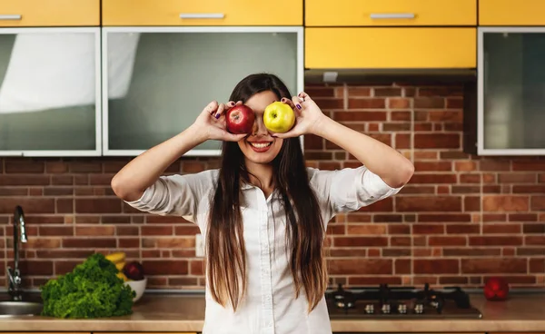 Wanita berambut cokelat muda di dapur menutup matanya dengan dua apel, merah dan kuning. Sehat makan dan konsep diet — Stok Foto