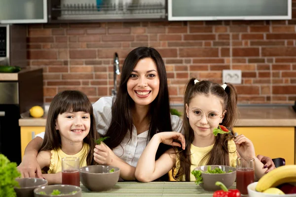 Gut gelaunte Mutter und zwei Töchter essen zu Hause gemeinsam gesunden Salat. Das Konzept der gesunden Ernährung, Familienwerte, gemeinsame Zeit — Stockfoto