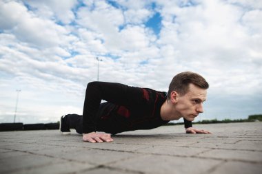 Spor sahasının asfaltında güçlü bir genç adam şınav çek. Adam sabahları antrenman yapıyor. Sağlıklı yaşam tarzı, spor anlayışı. Boşluğu kopyala.