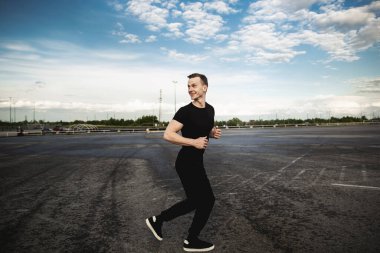 Stadyumun yakınında koşan ve gülümseyen bir sporcu. Adam dışarıda antrenman yapıyor. Maratona hazırlanıyorum..