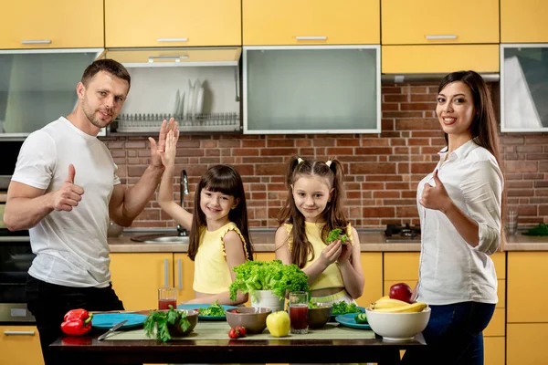 Potret keluarga bahagia, ayah ibu dan dua anak perempuan, memasak salad di dapur di rumah. Konsep makan yang sehat. Orangtua menunjukkan tanda tangan super — Stok Foto