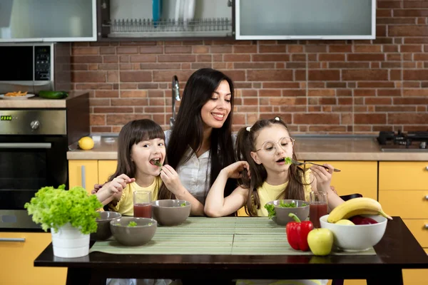 Ibu yang ceria dan dua anak perempuan sedang makan salad sehat bersama di rumah. Konsep makan sehat, nilai-nilai keluarga, waktu bersama — Stok Foto