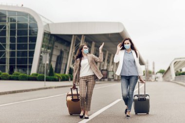 Coronavirus karantinasından sonra koruyucu maskeli iki mutlu kadın havaalanına gider. Havaalanına yakın genç kadınlar, hava yolculuğu, seyahat konsepti