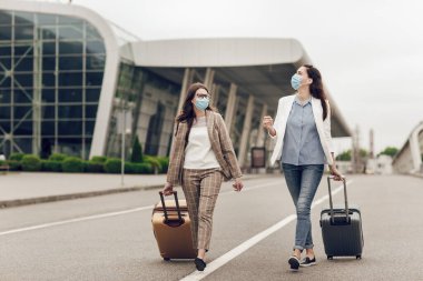 Coronavirus karantinasından sonra koruyucu maskeli iki mutlu kadın havaalanına gider. Havaalanına yakın genç kadınlar, hava yolculuğu, seyahat konsepti