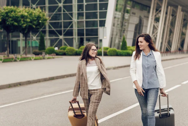 Dua perempuan rekan kerja kembali dari perjalanan bisnis bersama. Wanita muda dalam pakaian bisnis dengan koper di jalan — Stok Foto
