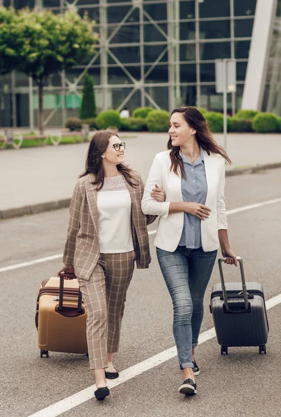 Dois amigos felizes sorridentes com malas perto do aeroporto. Mulheres colegas de trabalho que regressam de uma viagem de negócios conjunta — Fotografia de Stock