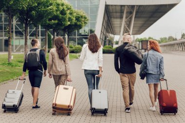 Bagajı dışarıda olan pozitif gençlerin arka görüntüsü. Arkadaşlar tatile gitmek için havaalanına giderler.