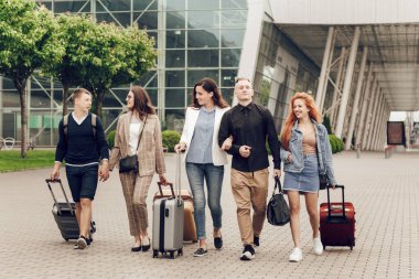 Havaalanı yakınlarında bavulları olan mutlu, pozitif genç insanlar. Seyahatten dönen arkadaşlar. Seyahat ve tatil kavramı
