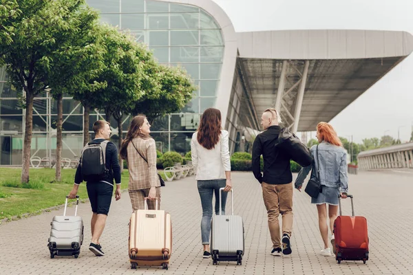 Pandangan belakang orang-orang muda positif dengan bagasi di luar ruangan. Teman-teman pergi ke bandara untuk berlibur. — Stok Foto