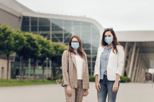 Dua wanita muda di latar belakang bangunan di luar, dengan masker medis di wajah mereka. — Stok Foto