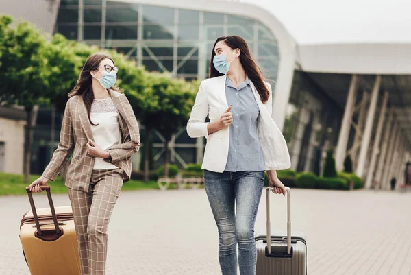 Dua wanita bisnis bertopeng pelindung dengan koper di dekat bandara. Perjalanan bisnis selama karantina coronavirus — Stok Foto
