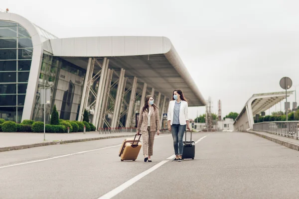 Two young women with suitcases return from a business trip during quarantine. Women with protective masks