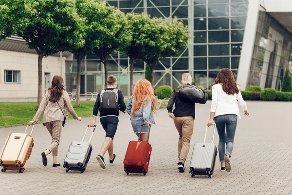 Pandangan belakang orang-orang muda positif dengan bagasi di luar ruangan. Teman-teman pergi ke bandara untuk berlibur. — Stok Foto