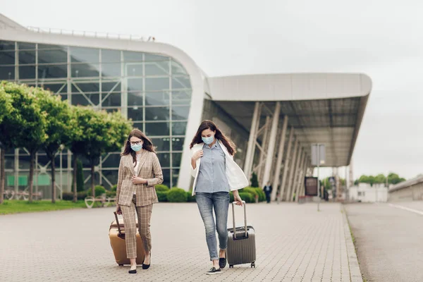 Two young women with suitcases return from a business trip during quarantine Stock Photo