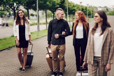 Ön manzara, mutlu genç insanlar, üç kadın ve havaalanı yakınlarında bagajlı bir adam.