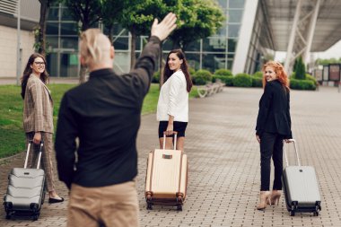 Havaalanında bir adam valizli üç mutlu kadına eşlik ediyor..