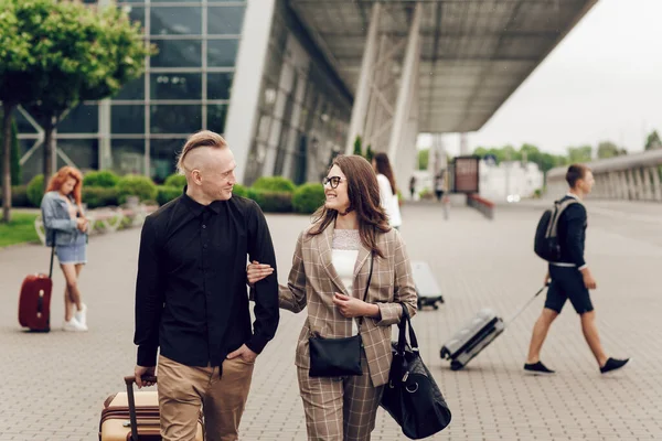 Casal jovem, homem e mulher perto do aeroporto com uma mala. Um casal feliz a viajar. Jovens que regressam de uma viagem — Fotografia de Stock