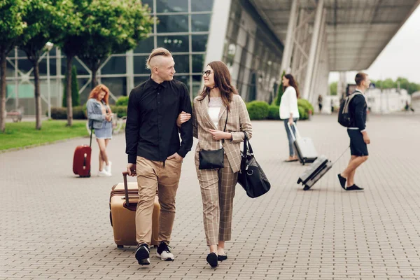 Pasangan muda, pria dan wanita di dekat bandara dengan koper. Pasangan bahagia bepergian. Anak muda kembali dari perjalanan — Stok Foto
