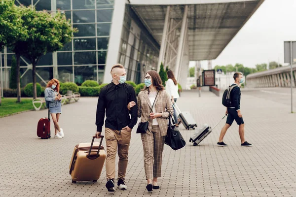 Joven hombre y mujer en máscaras protectoras con una maleta ir al aeropuerto. Viaje seguro después de una pandemia de coronavirus. —  Fotos de Stock