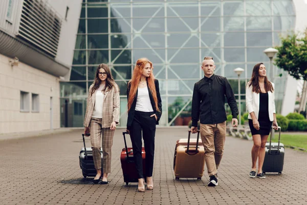 Pandangan di depan, orang-orang muda yang positif bahagia, tiga wanita dan seorang pria dengan bagasi di luar dekat bandara — Stok Foto