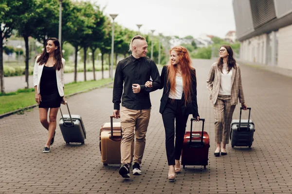 Pandangan di depan, orang-orang muda yang positif bahagia, tiga wanita dan seorang pria dengan bagasi di luar dekat bandara. — Stok Foto