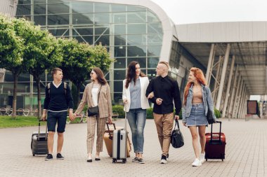 Havaalanı yakınlarında bavulları olan mutlu, pozitif genç insanlar. Seyahatten dönen arkadaşlar. Seyahat ve tatil kavramı