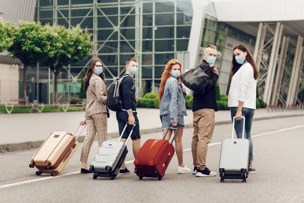 Vista trasera, jóvenes estudiantes en máscaras protectoras con maletas van a estudiar al extranjero después de la cuarentena del coronavirus. —  Fotos de Stock