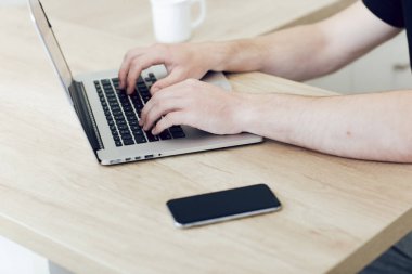 Dizüstü bilgisayarda yazan genç bir adamın ellerine yakın çekim. Mesafeli çalış, serbest çalışan evden çalışır. Gazetecilik karantina sırasında kendini izole eden bir makale yazar.